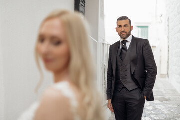 Closeup portrait blurred bride in foreground and handsome groom look at female with love and tenderness. Trendy clothes