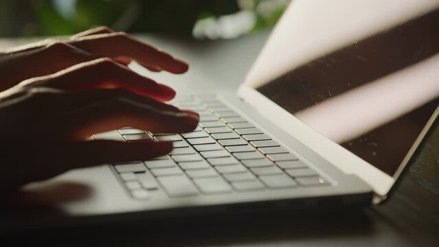 Close up of woman hands typing code on a laptop in 90 fps slow motion on a sunset sun