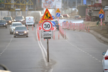 Roadworks warning traffic signs of construction work on city street and slowly moving cars
