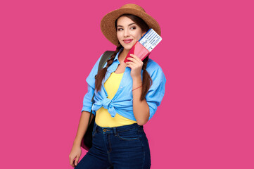 Smiling woman traveler in straw hat and backpack holding passport with plane ticket over pink isolate background