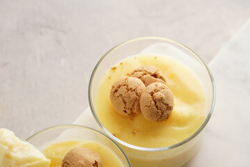 Creamy french vanilla pudding in glass decorated with italian biscuits amaretti on marble board on grey neutral background