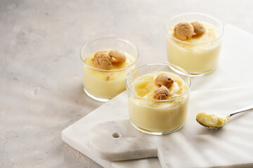 Creamy french vanilla pudding in glass decorated with italian biscuits amaretti on marble board on grey neutral background
