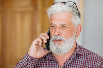 man with gray hair is working in an office on a laptop and talking on the phone. an adult male director or businessman is negotiating on an online webcam. business and finance of a male lawyer or