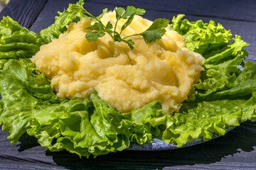 Mashed potatoes are laid out on lettuce leaves. Side dish of potatoes for meat or fish dish. On black background