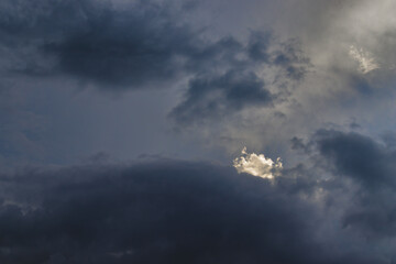 small white cloud illuminated by the sun, jutting out in a sky covered by gray clouds.
