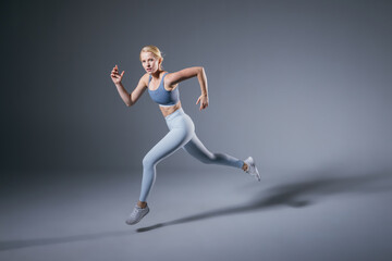 Women running in studio. Female runner on blue gray background. Healthy blonde woman. Profile view...
