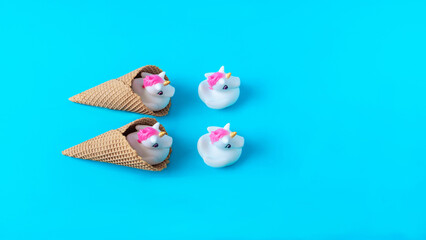 White and pink plastic unicorns coming out of ice cream cones against pastel blue background. Minimal surreal concept for summer holidays banner or card. Flat lay. Copy space.