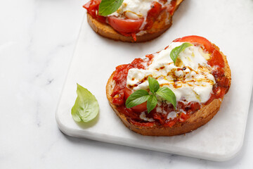 Bruschetta with stracciatella cheese, tomatoes and basil leaves on marble table