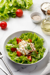 Green Salad with lettuce leaves, tomatoes, stracciatella cheese and sauce.  Keto diet, healthy and detox food concept. Vegetable salad bowl.