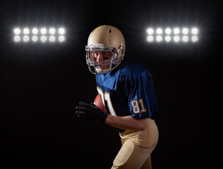 Young football player in running action on a dark background with stadium lights