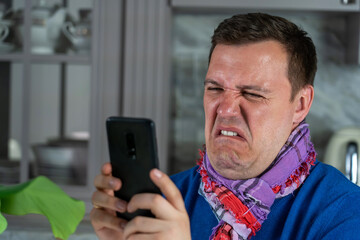 Obraz na płótnie Canvas Annoyed millennial man with disgust look at smartphone screen at modern kitchen. Portrait of manager cringe and looking at phone screen with squeamishness, bad joke or inappropriate content.