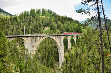 Wiesener Viaduct in the Davos mountains near Filisur. Beautiful old stone bridge with a moving train. Spring Time