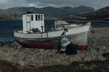 A girl in a black dress with moth wings poses against the background of an old ship