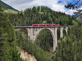 Fototapeta na wymiar Wiesener Viaduct in the Davos mountains near Filisur. Beautiful old stone bridge with a moving train. Spring Time