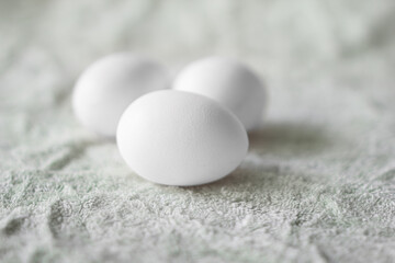 Three white eggs on light green fabric. Copy space. Selective focus on front egg.