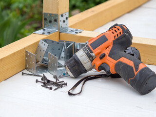 screwdriver, self-tapping screws and metal corners in the workplace, the concept of assembling a wooden house