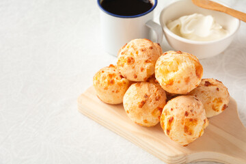 Minas Gerais cheese bread, hot, with a cup of black coffee and cream cheese, on a white tablecloth,...