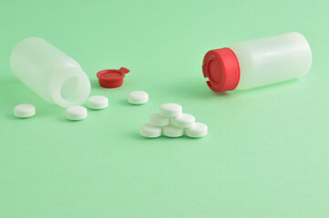 Close up, medication, rounded white tablets and small bottles on a green background.