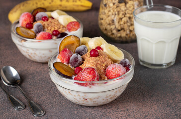 Granola crispy muesli with natural yogurt, frozen berries and fruit and nuts in two glass bowls on brown background, healthy breakfast