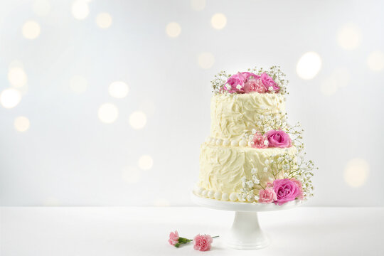 Wedding, Birthday 2 Tiered Cake for Cake Topper Mockup. Styled with fresh pink roses and gypsophila flowers, against a white background with bokeh party fairy lights.