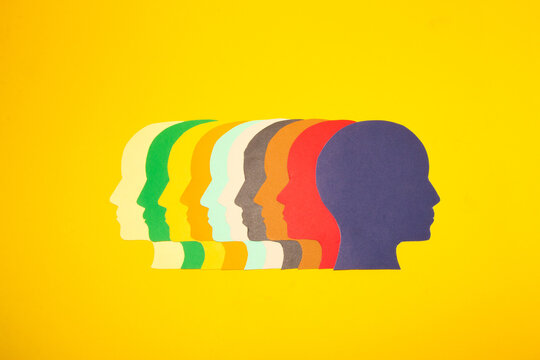 colorful paper heads facing left and the last blue head turned in the opposite direction, creative sobering solutions, individuality, yellow background