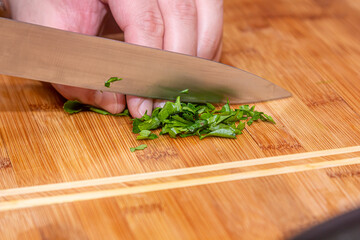 Cutting green parsley on a cutting board with a knife for cooking vegetarian food. Peasant food