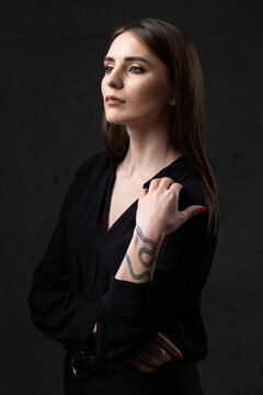 Portrait of a young brunette with long hair in the studio. Dramatic photo in dark colors. A girl with a snake tattoo on her arm.