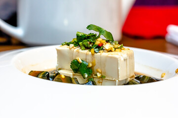 Silk tofu japanese soy cheese whole piece with chili ginger, chive and soy sauce topping on ceramic plate over wooden table