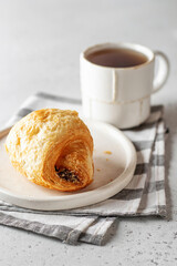 Morning concept. Fresh croissant on white plate on napkin with tea on light background