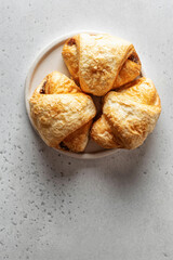 Three fresh croissants on a white plate on light background, top view