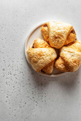 Three fresh croissants on a white plate on light background, top view