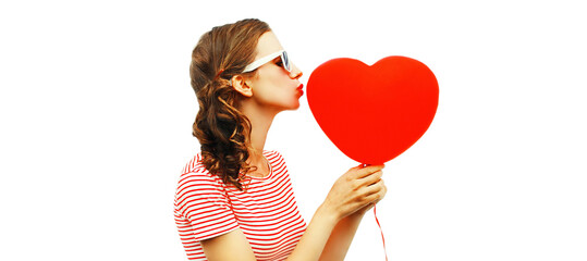 Portrait of beautiful young woman with red heart shaped balloon blowing her lips sending sweet air kiss isolated on white background