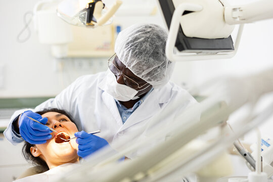 Portrait of focused qualified african american dentist with female patient during oral checkup and teeth treatment in specialized dental office..