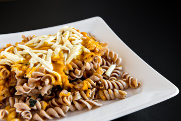 Fusilli pasta with pumpkin sauce and colonial cheese on black background.