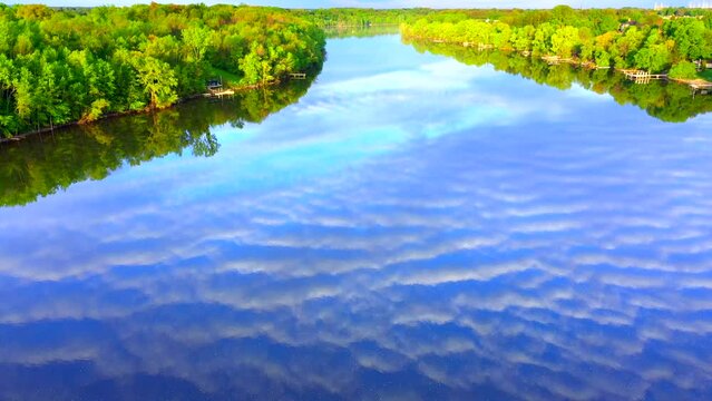 Amazing sky with rippled clouds, mirrored in tranquil river at daybreak, moving aerial view.
