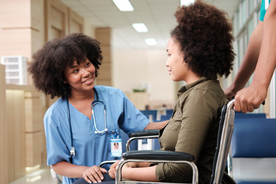 Young African American female doctor with stethoscope in uniform checks injury patient girl in wheelchair at outpatient accident clinic hospital, illness medical clinic examination, healthcare hall.