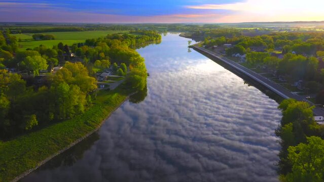 Amazing sky with rippled clouds, mirrored in tranquil river at daybreak, moving aerial view.
