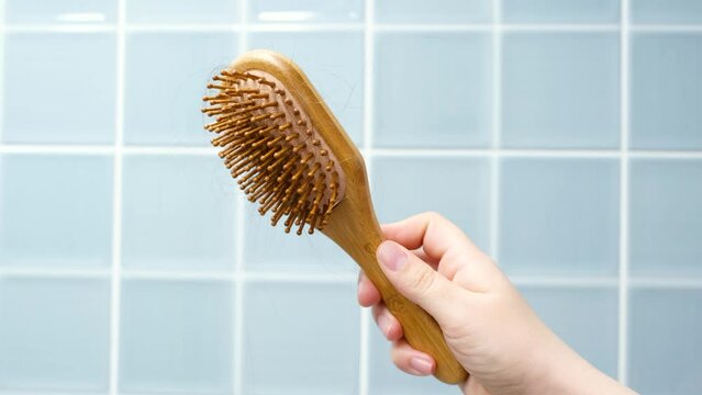 Female hand holding a comb with lost hair on background of blue tiles close-up.