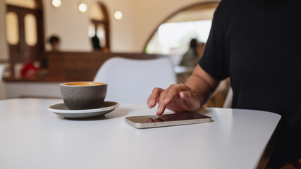 Closeup image of a woman using and touching on mobile phone screen with coffee cup on the table