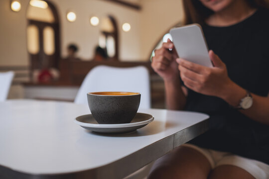 Closeup image of a young woman holding and using mobile phone with coffee cup on the table in cafe