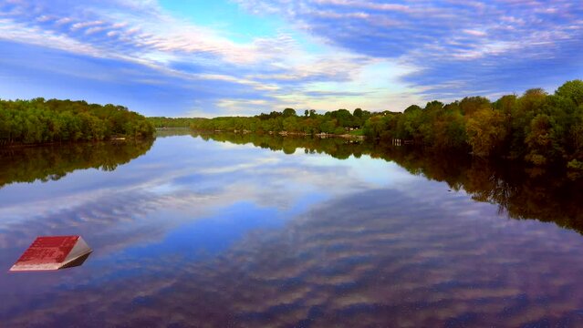 Amazing sky with rippled clouds, mirrored in tranquil river at daybreak, moving aerial view.
