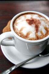 A cup of espresso cappuccino with a sprinkling of cinnamon powder. Additional sweet bread cake background and cinnamon sticks.