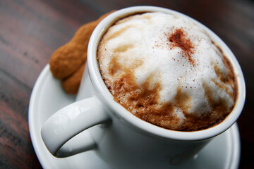 A cup of espresso cappuccino with a sprinkling of cinnamon powder. Additional sweet bread cake background and cinnamon sticks.