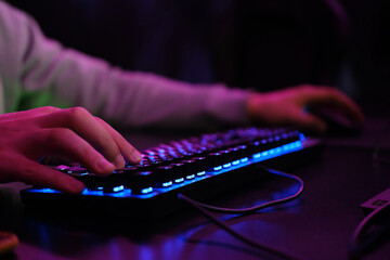 Selective focus on hand. Close up of cyber sportsman hands on gaming equipment. Cyber sport concept. The hacker uses the keyboard, shakes the buttons with his fingers to crack the password.Neon color 