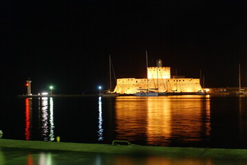 The Fort of Saint Nicholas at the mouth of the Mandraki harbour at night, on the island of Rhodes,...