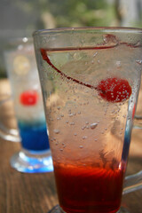 Two glasses of red and blue ice squash. Contains syrup, ice cubes and soda plus a cherry. There are small bubbles. background blur. refreshment.looks very fresh