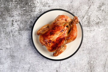 Homemade Whole roast chicken on a round plate on a dark gray background. Top view, flat lay