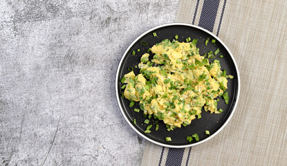 Scrambled eggs and scallions on a round plate on a dark gray background. Top view, flat lay
