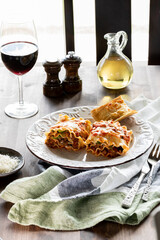 A gourmet meal of lasagna roll ups served with red wine. Lit from behind.