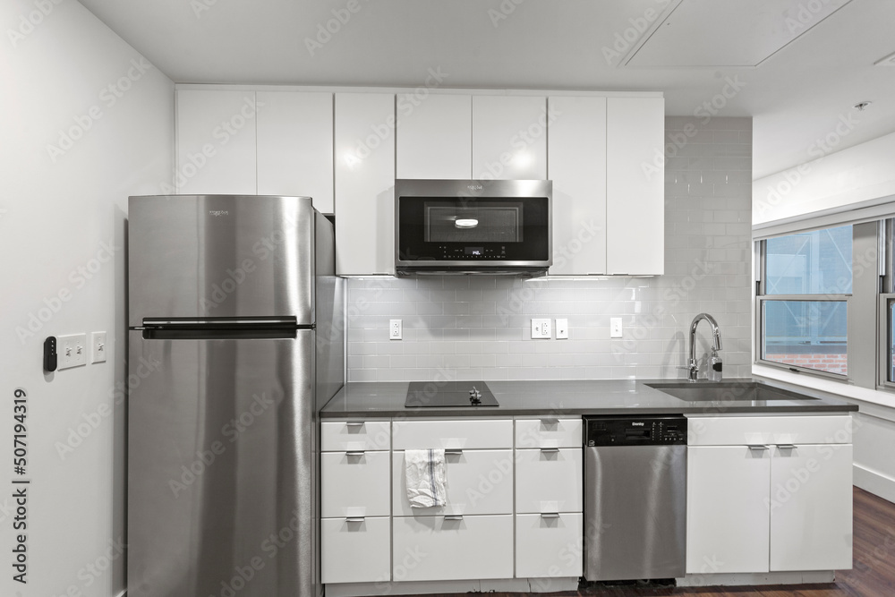 Wall mural White apartment kitchen with black counter tops and white cabinets in city apartment